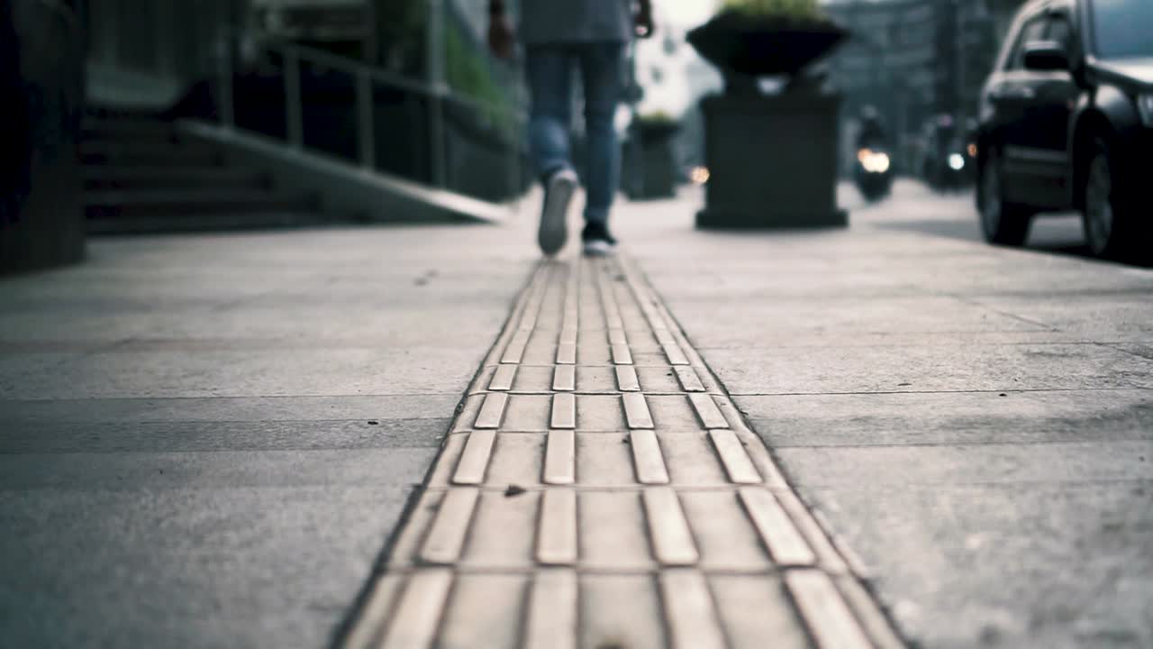 Low angle shot of man walking away, busy street, tactile tiles for blind people