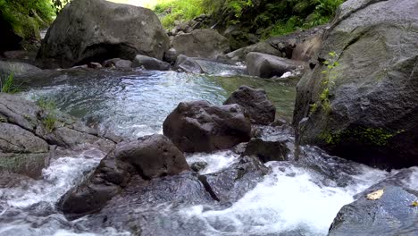 close up of a fresh, clear mountain river flowing over big brown mossy rocks and boulders in a tropical island rainforest