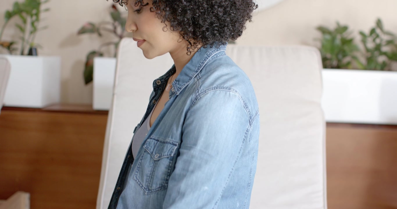 Donna afroamericana che entra, si siede su un cuscino da salotto con uno smartwatch e sistema le gambe per riposare.