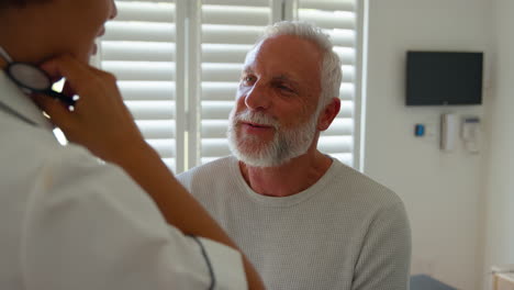 Female-Nurse-Wearing-Uniform-Listening-To-Senior-Male-Patient's-Chest-In-Private-Hospital-Room