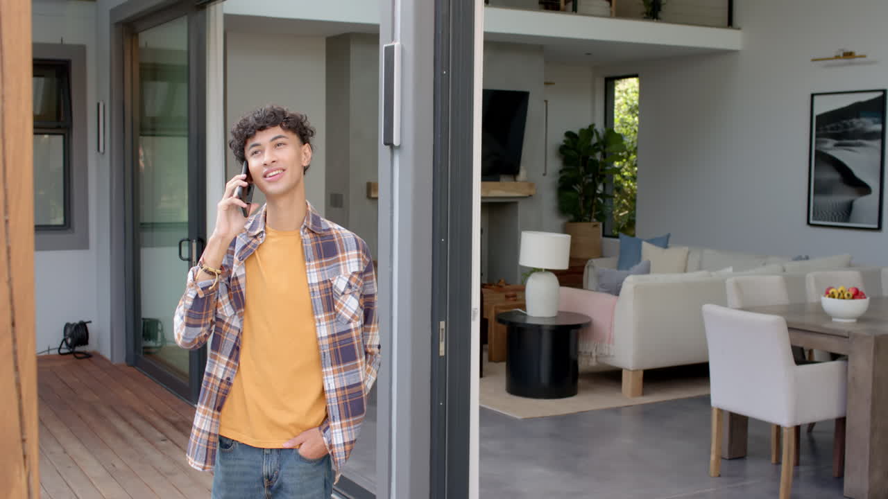 Talking on smartphone, teenage boy standing in doorway of modern home