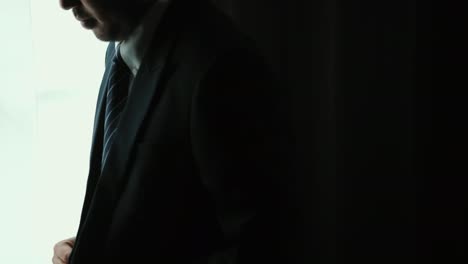 confident businessman adjust classic blue suit with necktie near window in hotel room. handsome man wearing a nice suit on wedding day.