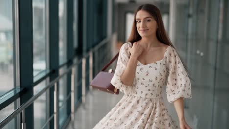 Hübsche-Nette-Frau,-Die-Sich-In-Einem-Kleid-Mit-Handtasche-Im-Glasflur-Dreht