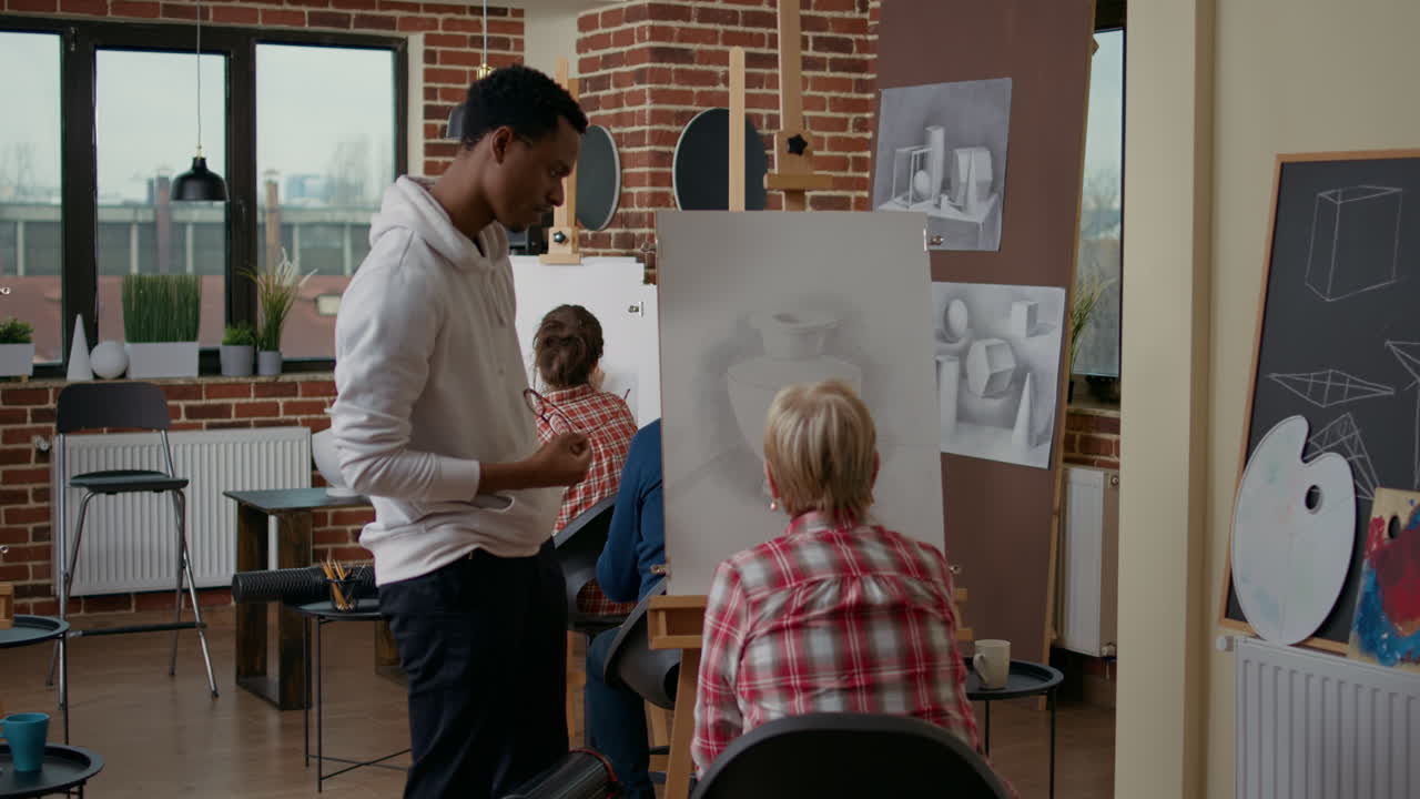 Male teacher looking at elder student drawing on canvas
