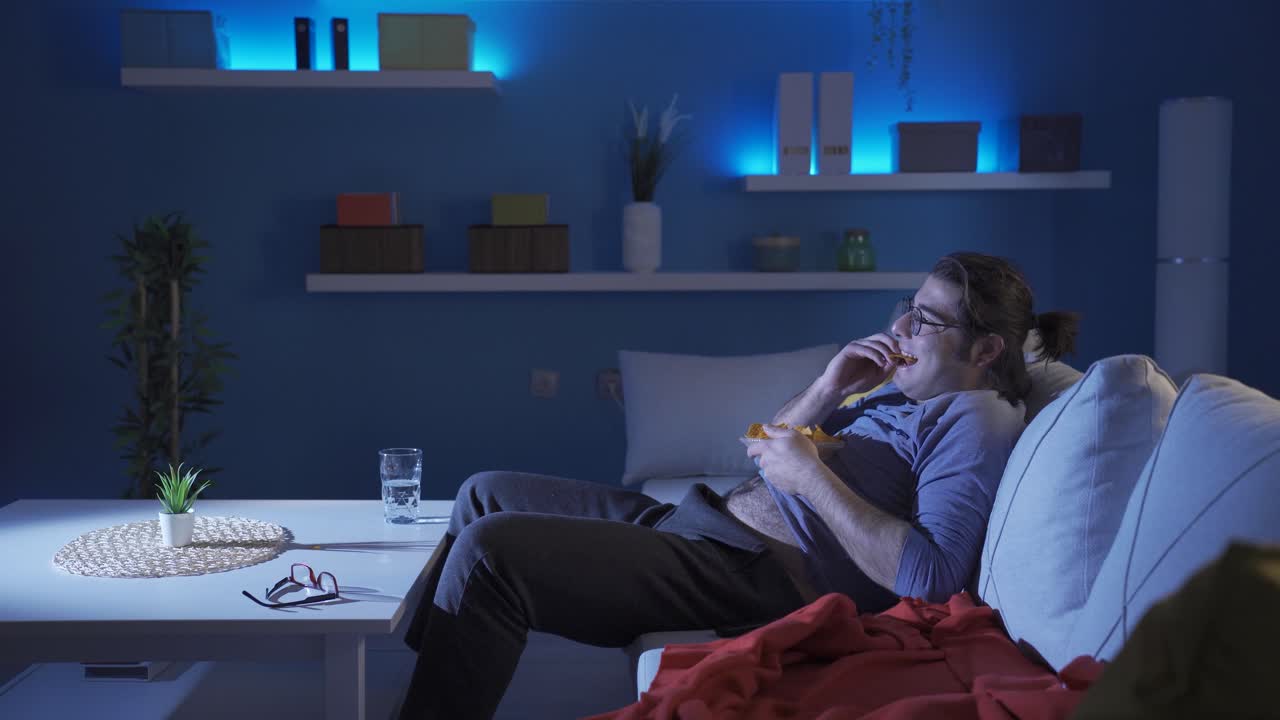 Uomo divertente mangia patatine e si gratta la pancia mentre guarda la TV