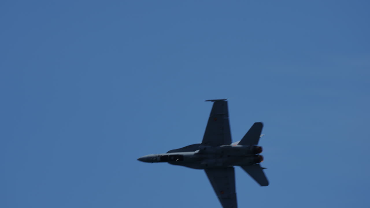 Military jet fighter performing a sharp left turn against clear blue sky