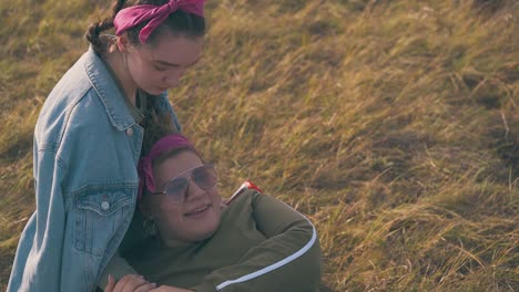 young women spend nice time on dry grass by camp at sunset