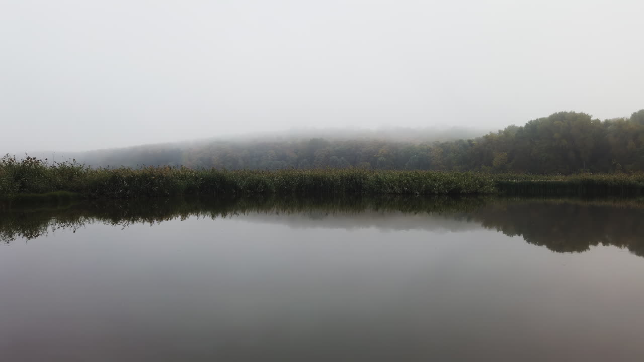 Tranquil landscape of a mist covered lake reflecting trees in soft morning light