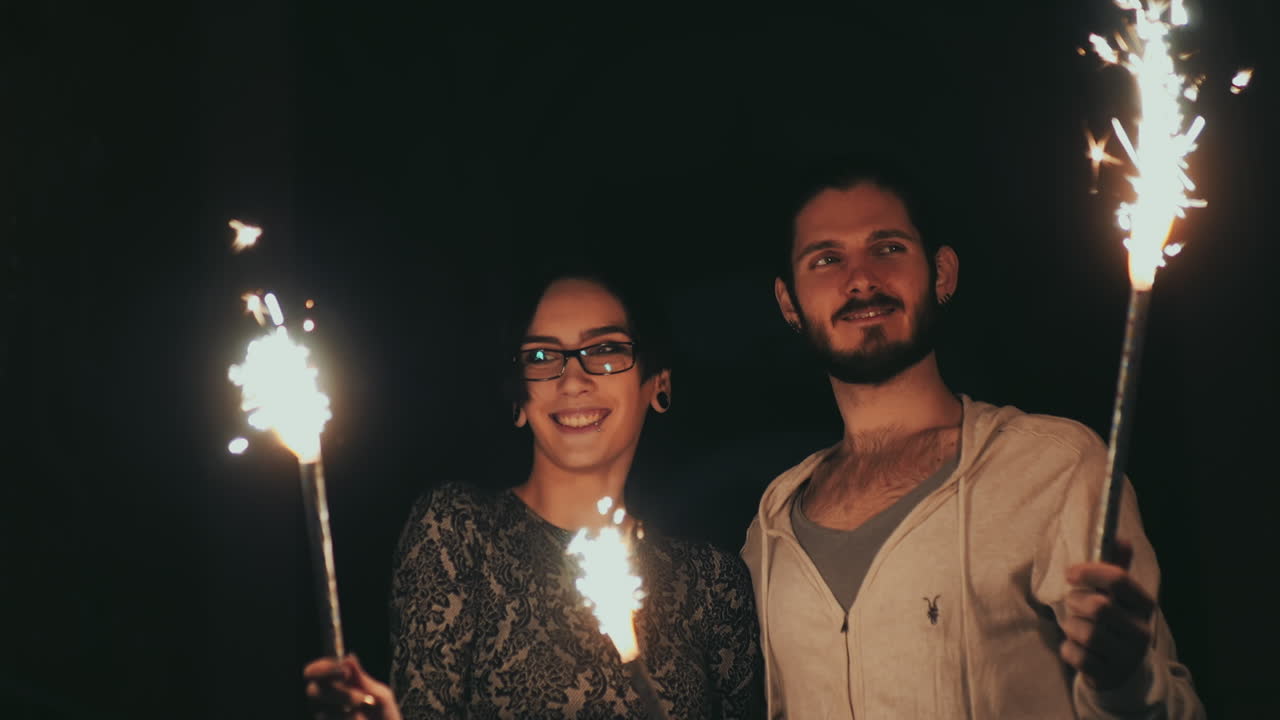 joven pareja hipster divirtiéndose con fuegos artificiales en manos de