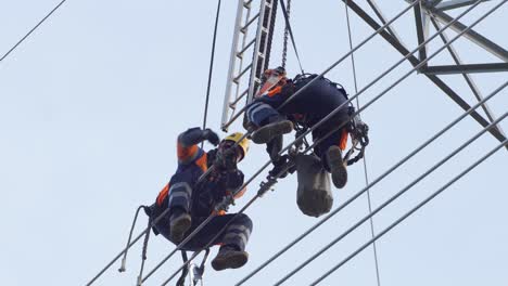 two maintenance technicians sit high up on power lines