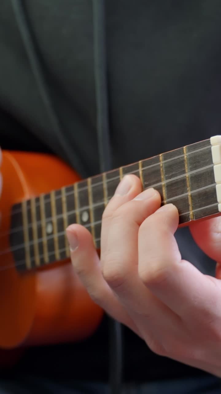 Man fingers playing guitar or ukulele, close up vertical view