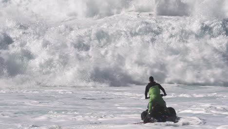 jetski driver and a surfer trying to ride the choppy waves full of white foam nazare, portugal