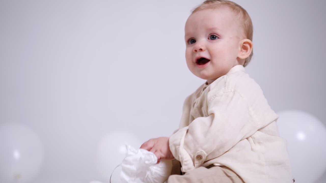 Lovely Caucasian child is given a bundle with a string. Adorable baby turns the bundle in hands playing with it. White backdrop.