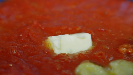 Primer-Plano-De-Mantequilla-Derritiéndose-En-Una-Salsa-De-Tomate-Roja