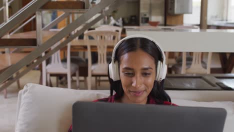 Mixed-race-woman-on-couch-at-home-using-laptop-listening-to-music
