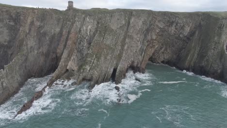 slow aerial dolly parellel to irish cliffs with rough seas and wave battering the clifs and birds flying