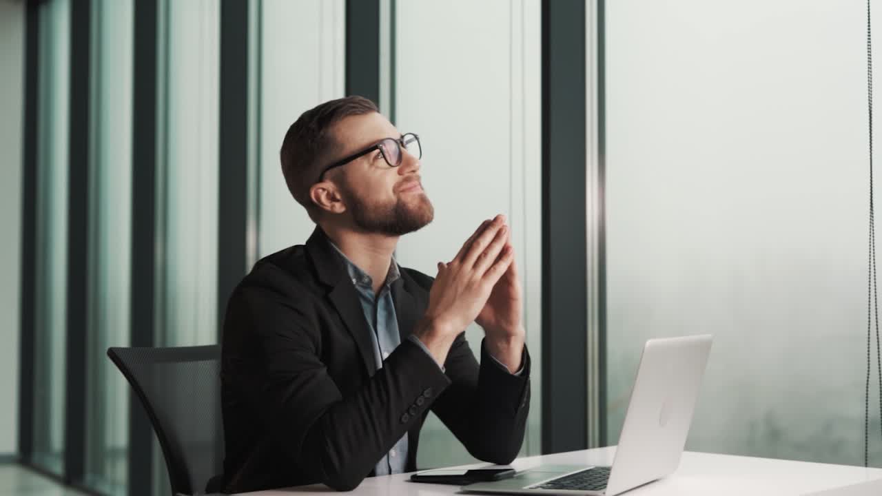 A dreamy man sitting at a table with a laptop thinks and looks out the window