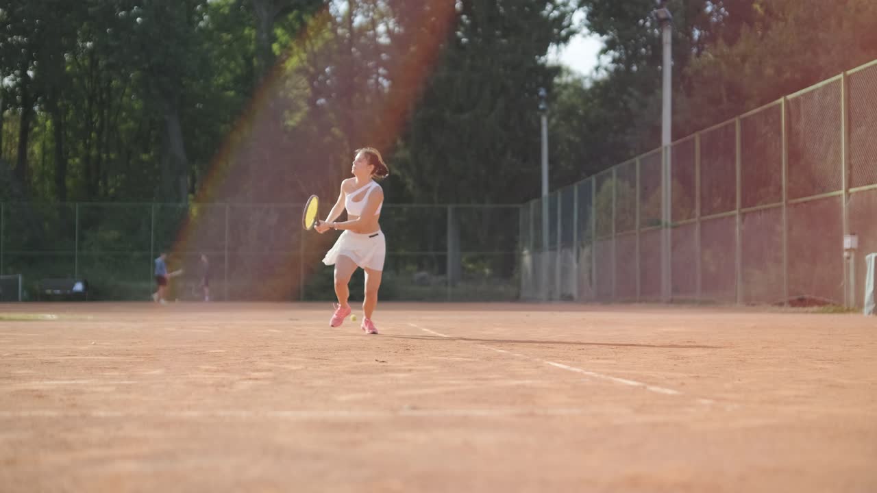 코치와 함께 야외 코트에서 테니스를 연습하는 젊은 여성. 코치는 선수가 그녀의 기술에 대해 일하면서, 운동 훈련 세션에서 그녀의 스트로크를 완성하는 동안 지침을 제공합니다.