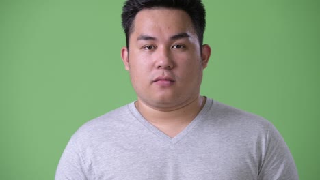 young handsome overweight asian man against green background