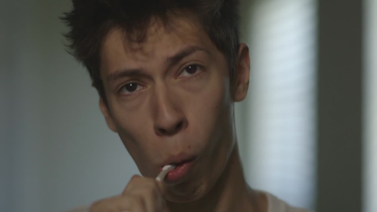 Young Caucasian Man Brushes Teeth Looking Straight at Camera