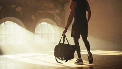 athlete man in black sportswear in summer uniform brings a backpack and lays out his fitness equipment in a sunny brick hall