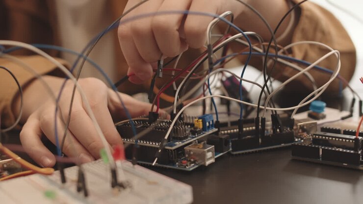 Hands connecting wires to an electronic circuit board