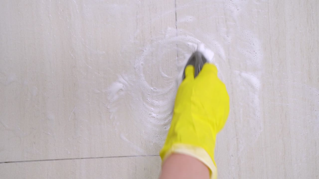 la mano humana en guante de protección amarillo limpiando la pared o el piso de cerámica, haciendo movimientos circulares con cepillo y limpiador de jabón o detergente. en el interior, deberes de limpieza concepto de movimiento lento.