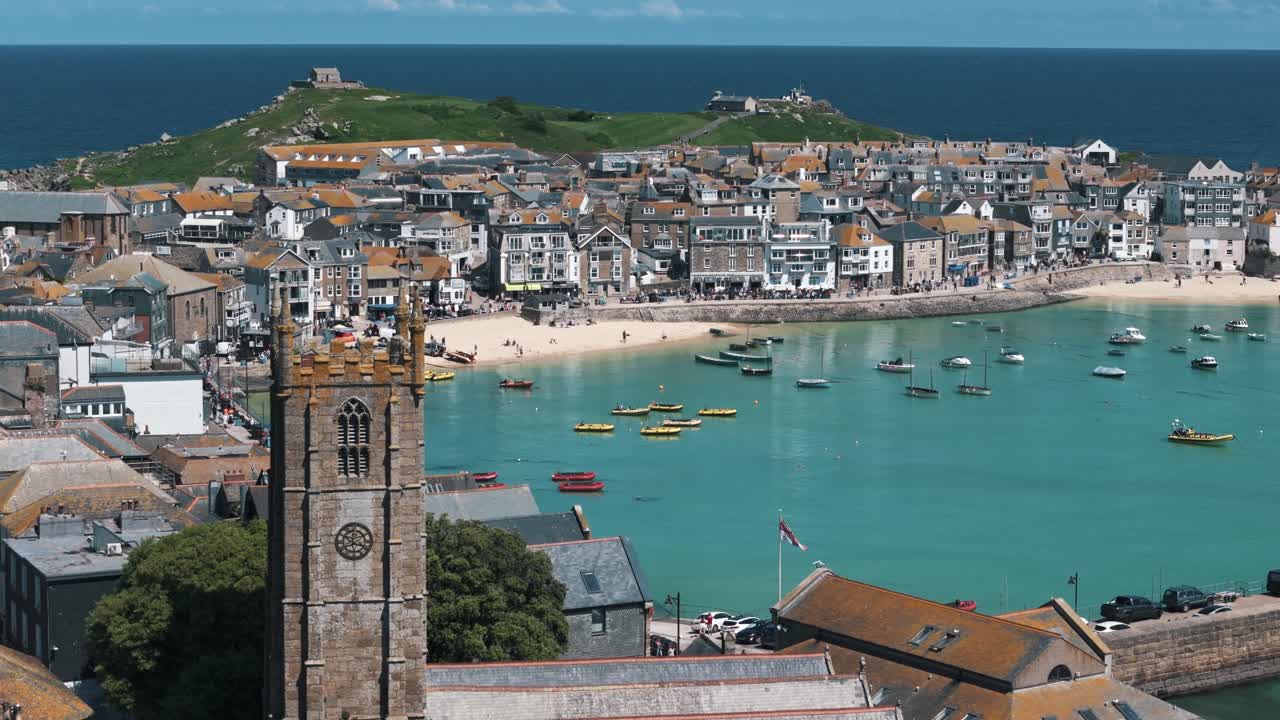 Dolly right over St Ives church with boats and bay in the distance beneath blue sky