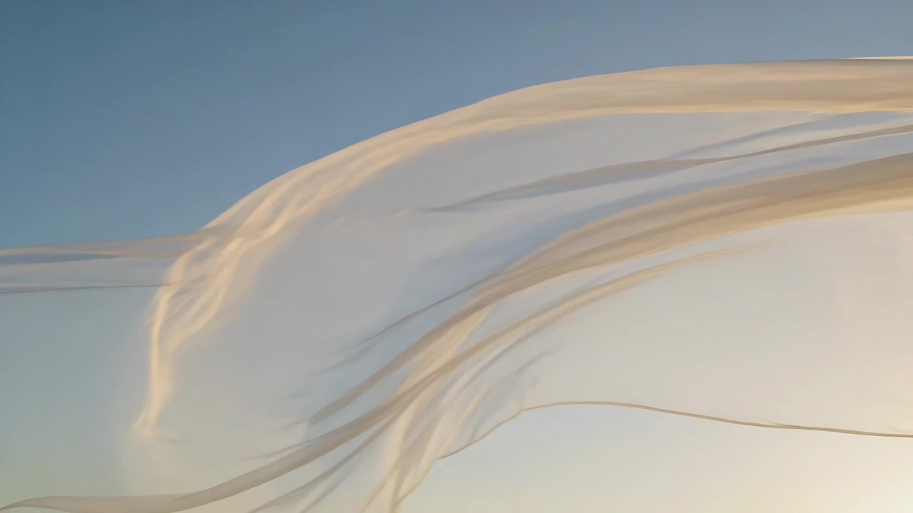 Grand voile léger flottant au gré d'une rafale, se déplaçant dans un ciel clair sous un soleil bas, révélant de fins rubans.