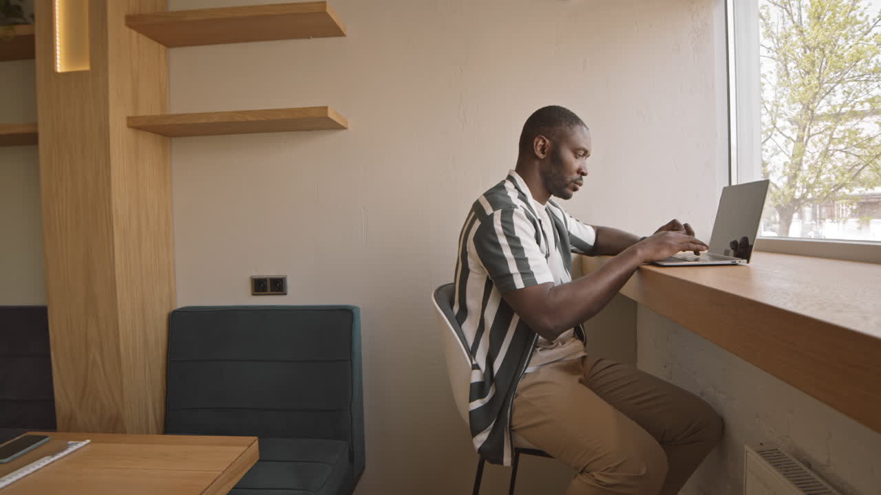 Afro American Freelancer Working on Laptop in Cozy Cafe