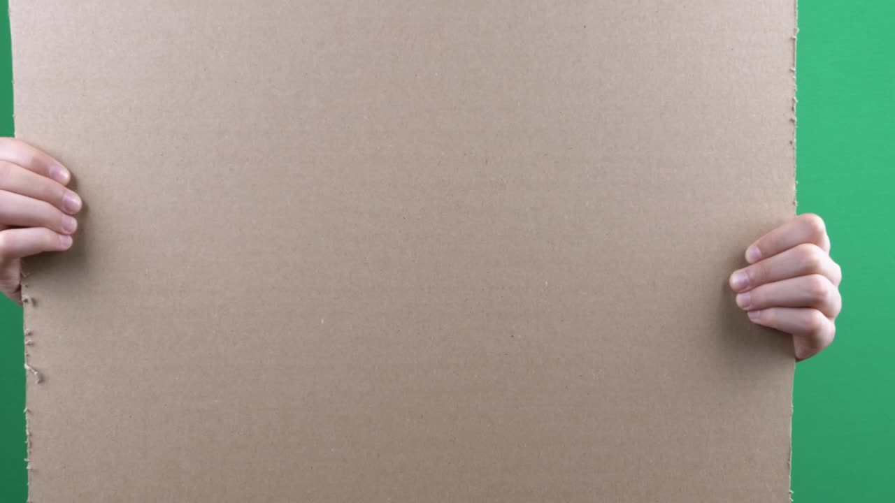 Boy holding in his hands blank empty cardboard poster on green chromakey screen background