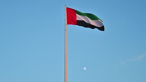 bandera de los emiratos árabes unidos ondeando en el aire, la luna en cuarto creciente en segundo plano, el símbolo nacional de los emiratos árabes unidos, día nacional de los emiratos árabes unidos 2020, vídeo de 4k