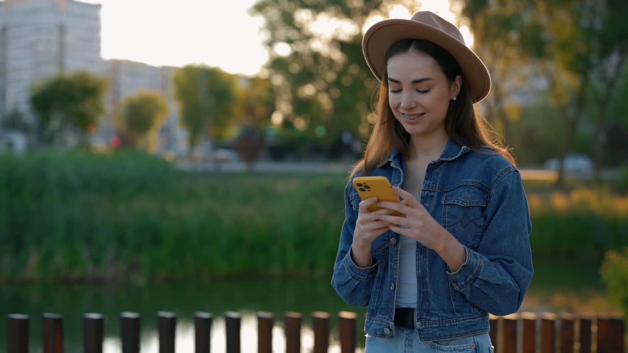 Young woman using a phone in a park at sunset
