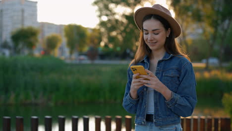 young woman using a phone in a park at sunset