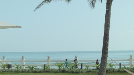 static shot of a beach with local kids walking and surfers in the background