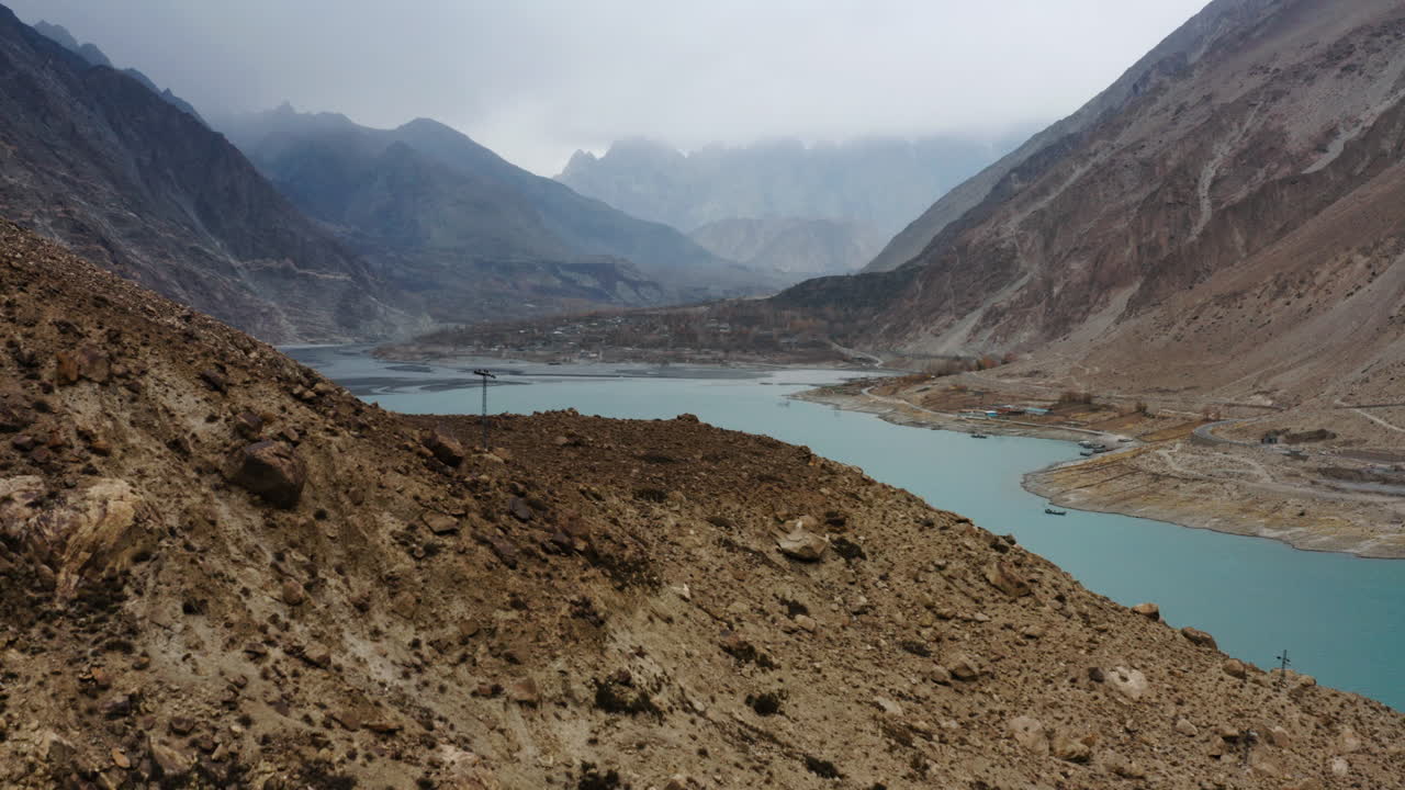 volando sobre la ladera de la montaña marrón junto al lago attabad en un día nublado, himalaya