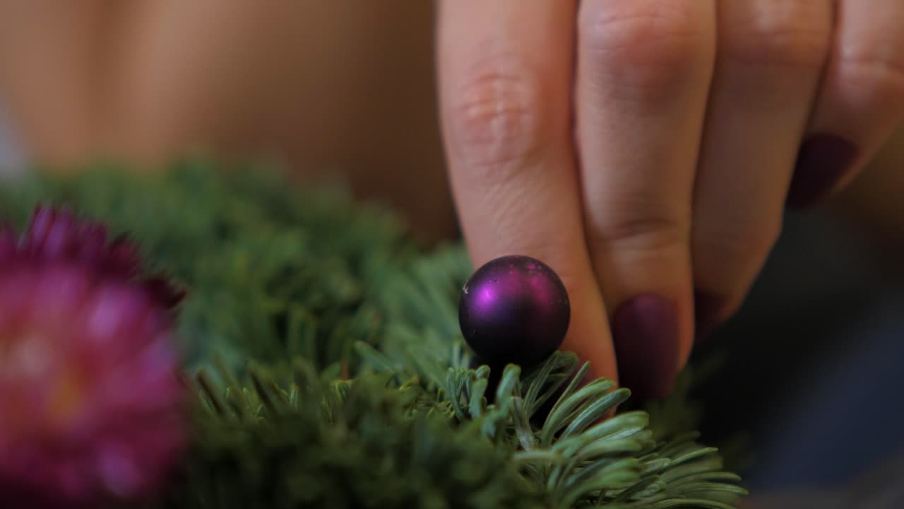 mujer haciendo una corona de abeto para la víspera de navidad y decorándola con una pequeña bola morada, decoración artesanal diy, tradiciones de invierno, vacaciones de temporada, manos de cerca
