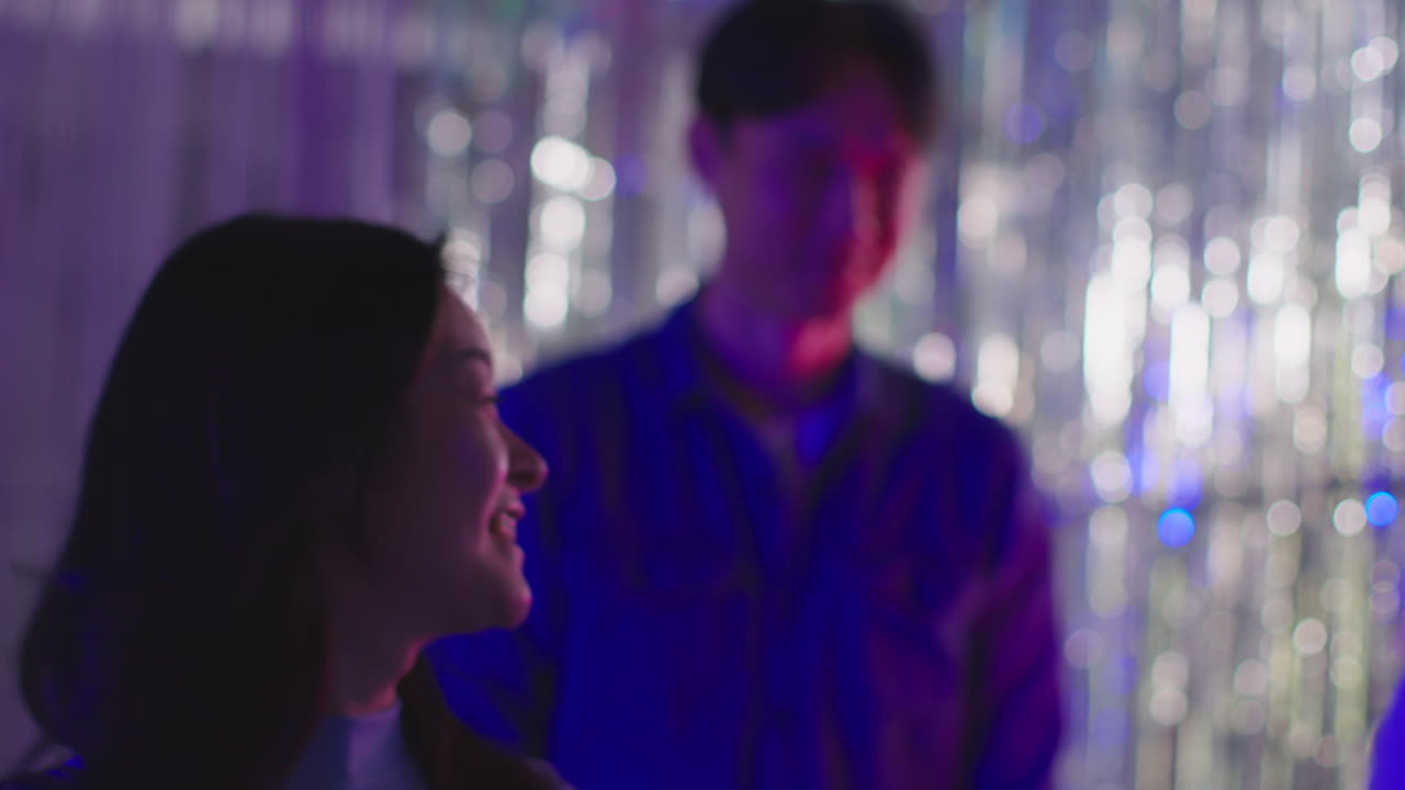 젊은 친구 들 의 그룹 이 나이트클럽 이나 파니페어 에서 틴셀 커튼 을 지나가고 있다