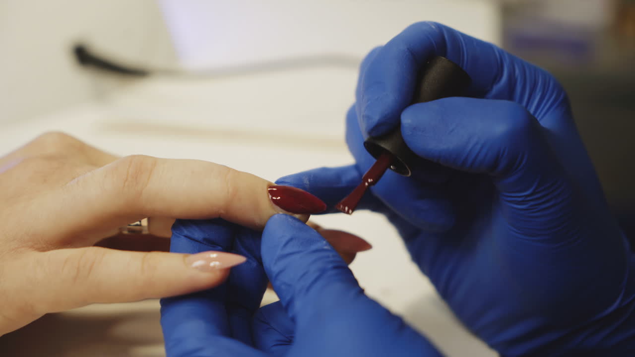 Master of manicure paints nails to the girl in the salon. Colored manicure. Close-up