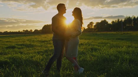 pregnant couple enjoying a sunset in a field