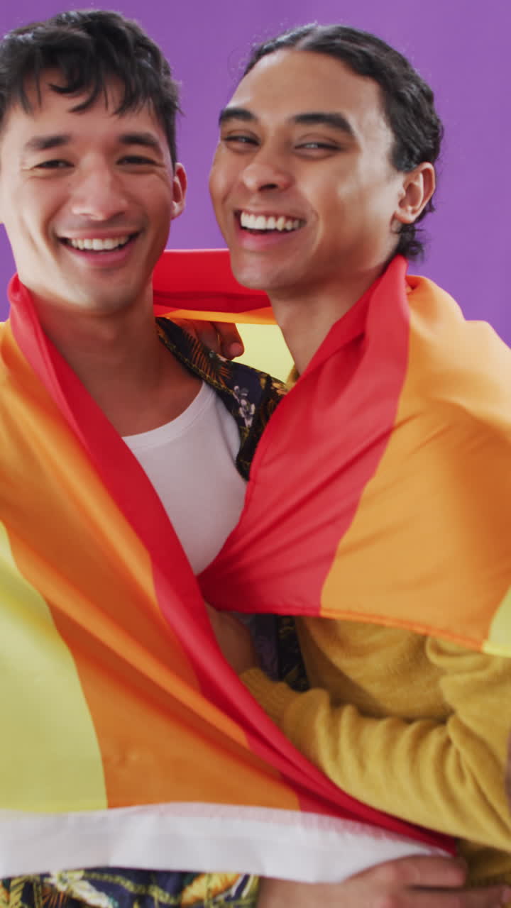 video vertical de retrato de una pareja feliz y diversa abrazando y sosteniendo una bandera lgbt