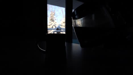 silueta de una taza de café y una olla con pinos nevados en la ventana