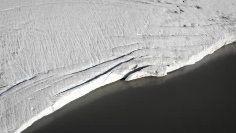 aerial flyover alongside the ice bordering the glacial lake of the claridenfirn glacier in uri, swizerland with noticeable crevasses and cracks in the ice