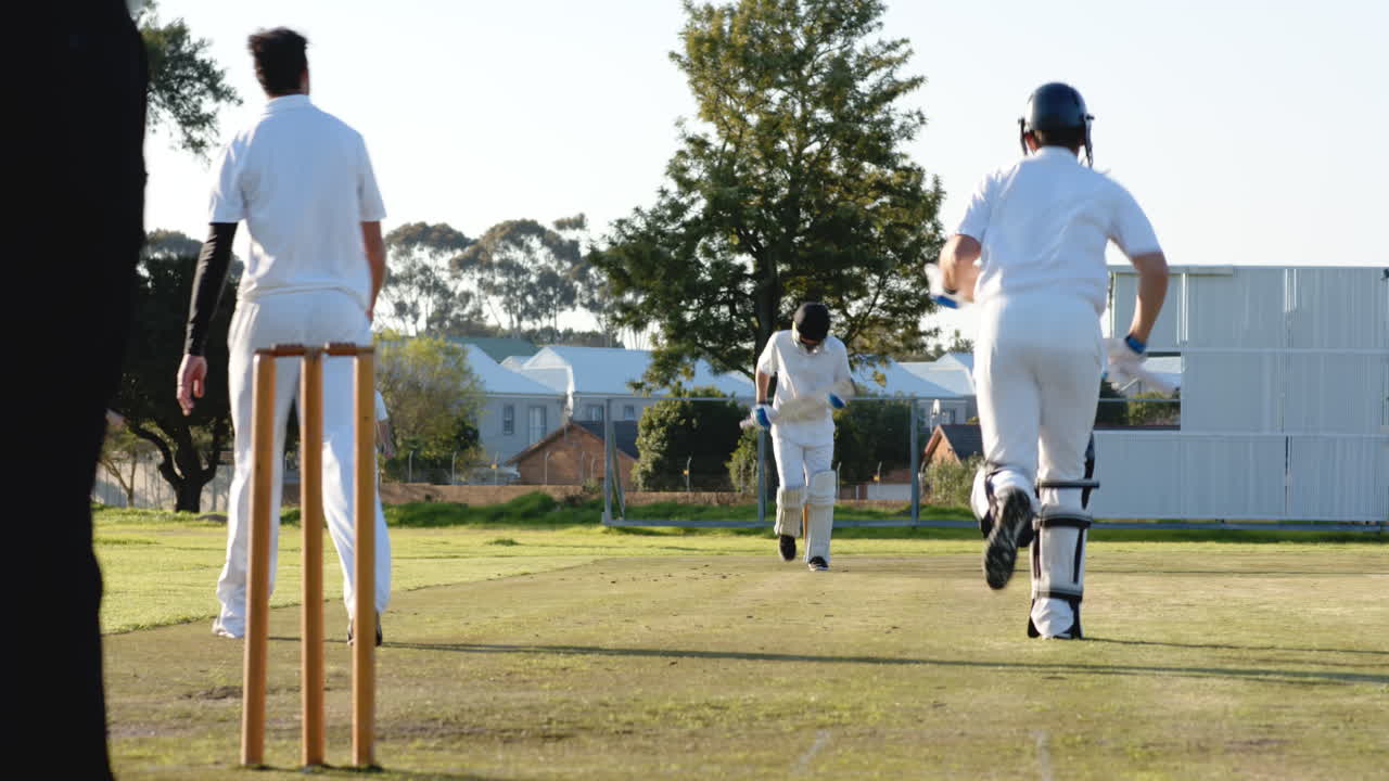 Two teams of multiracial male cricket players playing cricket, batters running with bats on pitch