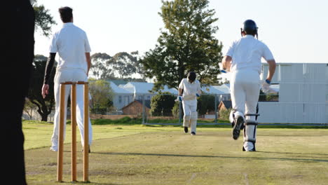 two teams of multiracial male cricket players playing cricket, batters running with bats on pitch