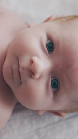 infant boy with short blond hair and large crystal blue eyes lies on changing table and looks at camera extreme closeup