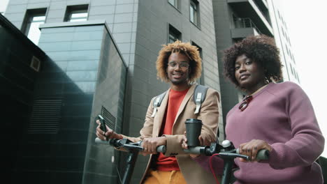 portrait of cheerful black man and woman with e-scooters in city