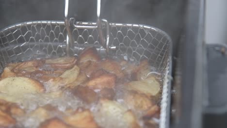 potato wedges frying in fryer with boiling hot oil, steam rising, close up