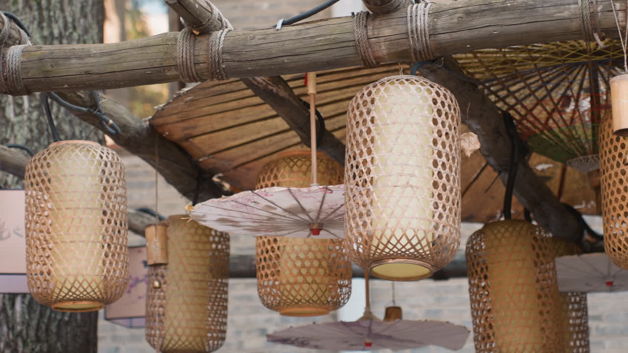Lanterne di bambù appese sotto una tettoia di legno in un ambiente di mercato artigianale, paralumi intrecciati e ombrelli di carta creano una texture calda, esposizione artigianale con toni tenui, la luce soffusa del giorno evidenzia i motivi intrecciati
