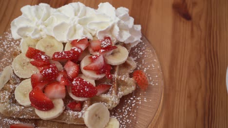 Gofre-Belga-Con-Fresas,-Plátano-Y-Crema-Batida-Movimiento-Panorámico-Lento-De-Postre-Dulce-En-La-Mesa-De-Madera